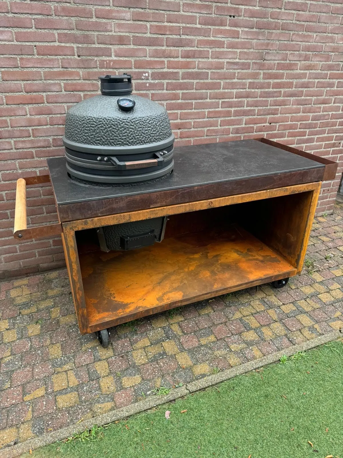 Buitenkeuken van cortenstaal met een kamado-barbecue, tegen een bakstenen muur