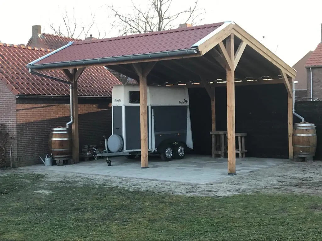 Houten carport met zadeldak, met een paardentrailer eronder