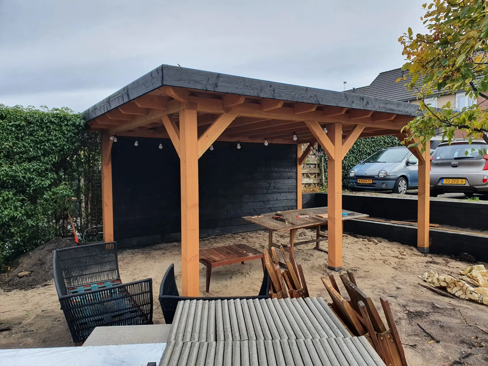 Houten overkapping in aanbouw, met het werkmateriaal nog in de tuin
