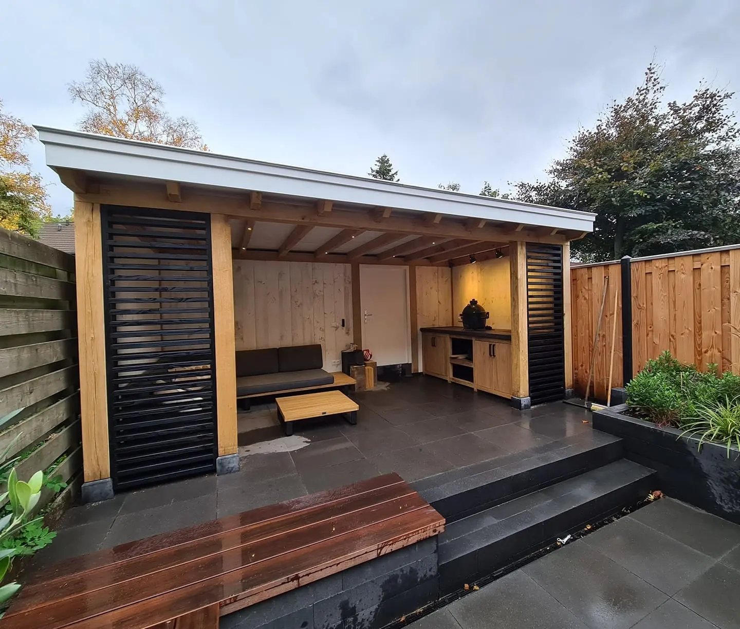 Overkapping met zwarte lamellen, een loungehoek en een houten vlonder