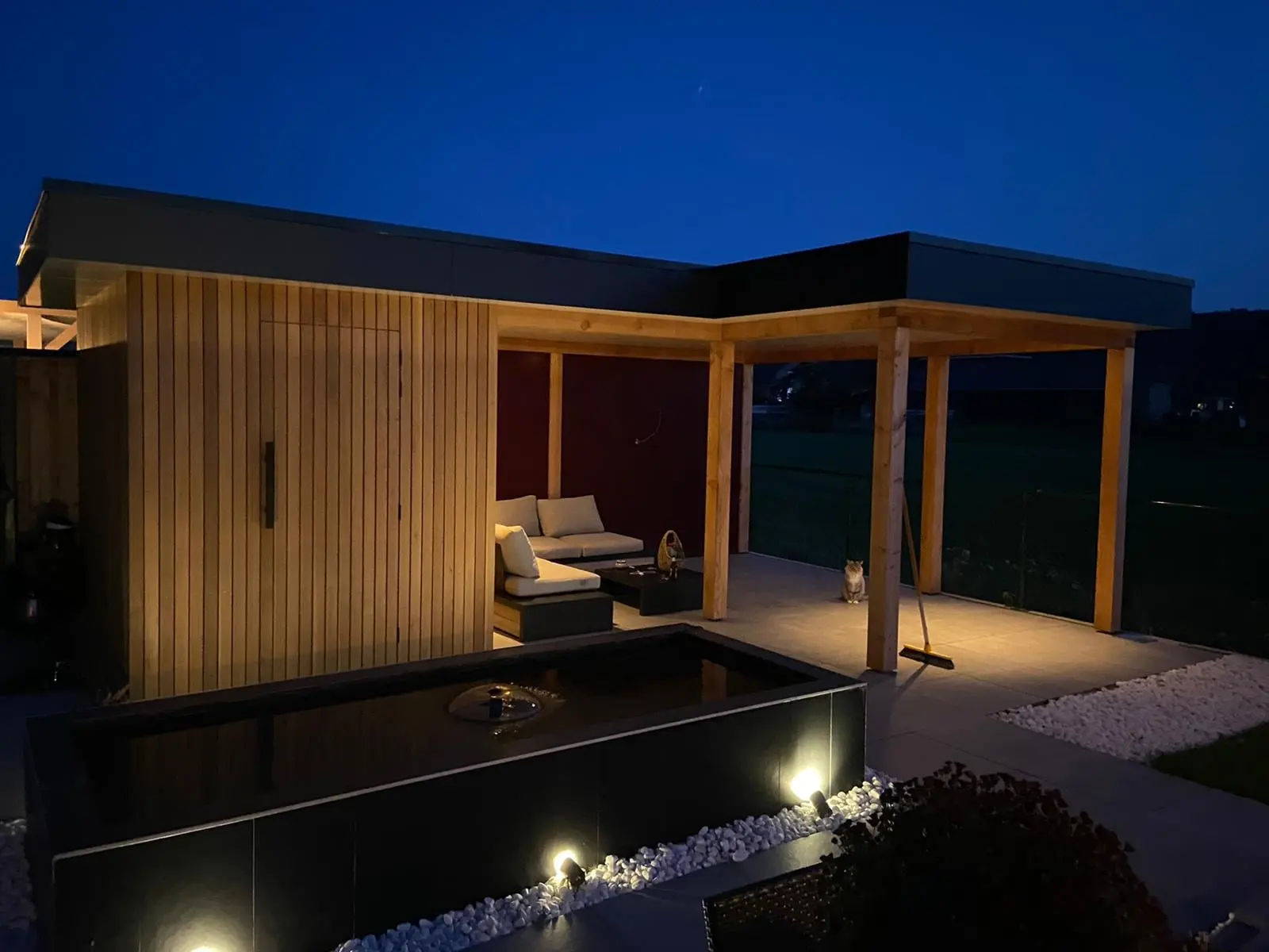 Tuinhuis met houten gevel en overkapping, ’s avonds verlicht