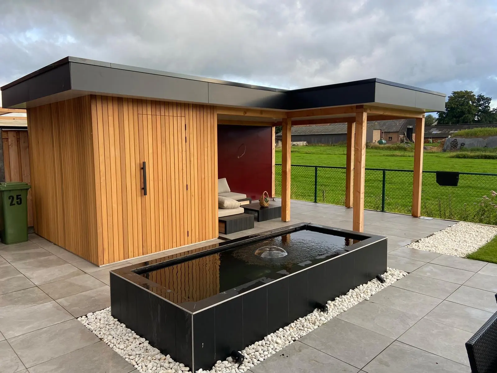 Tuinhuis met verticale houten gevelbekleding en een overkapping, met een verhoogde vijver op het terras