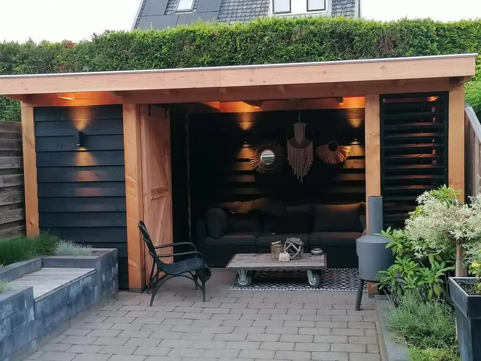 Overkapping met zwarte gevelbekleding, sfeerverlichting en een loungebank