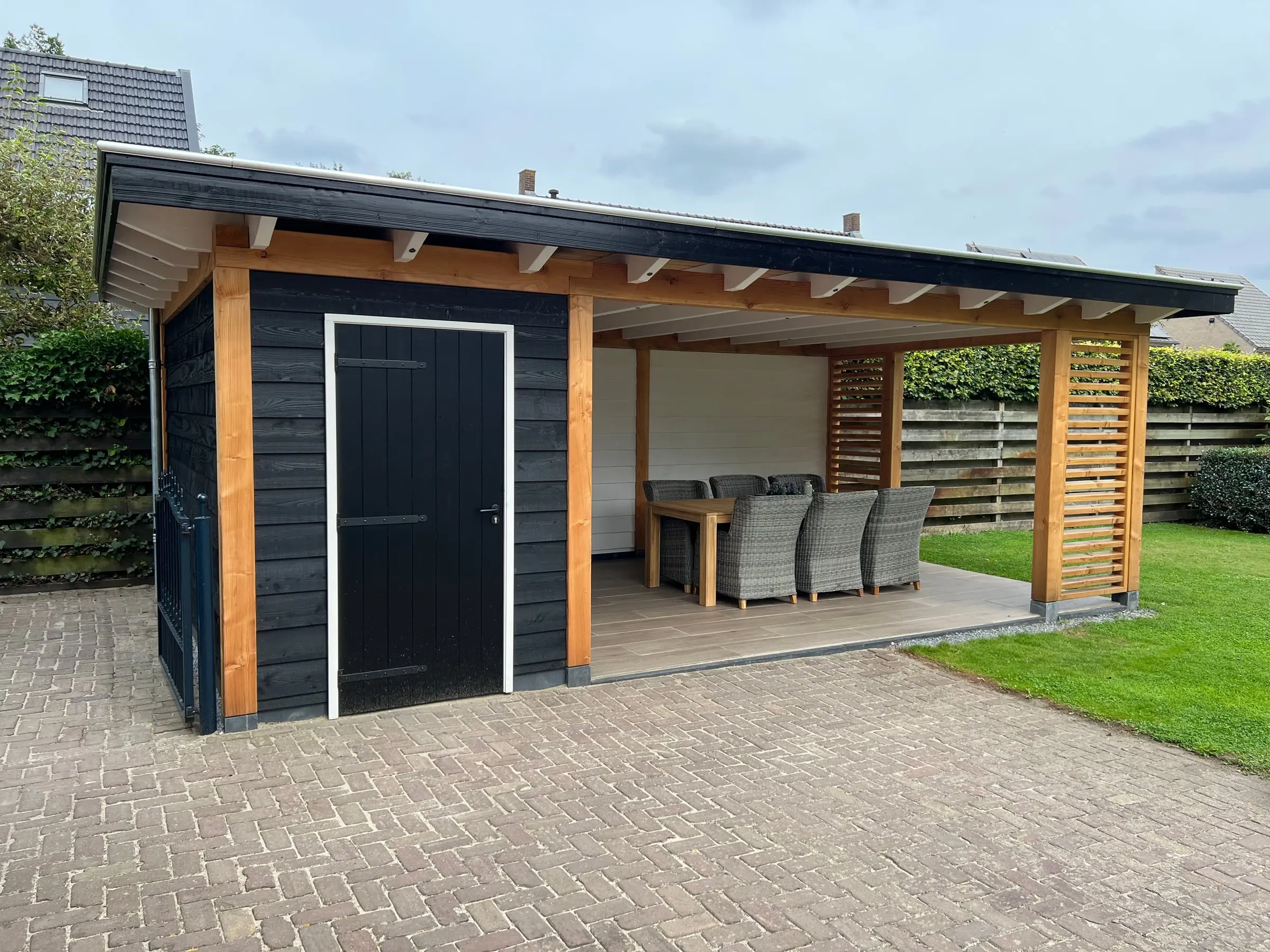 Zwart tuinhuis met een overkapping op houten staanders en een lamellenwand, in Raamsdonk
