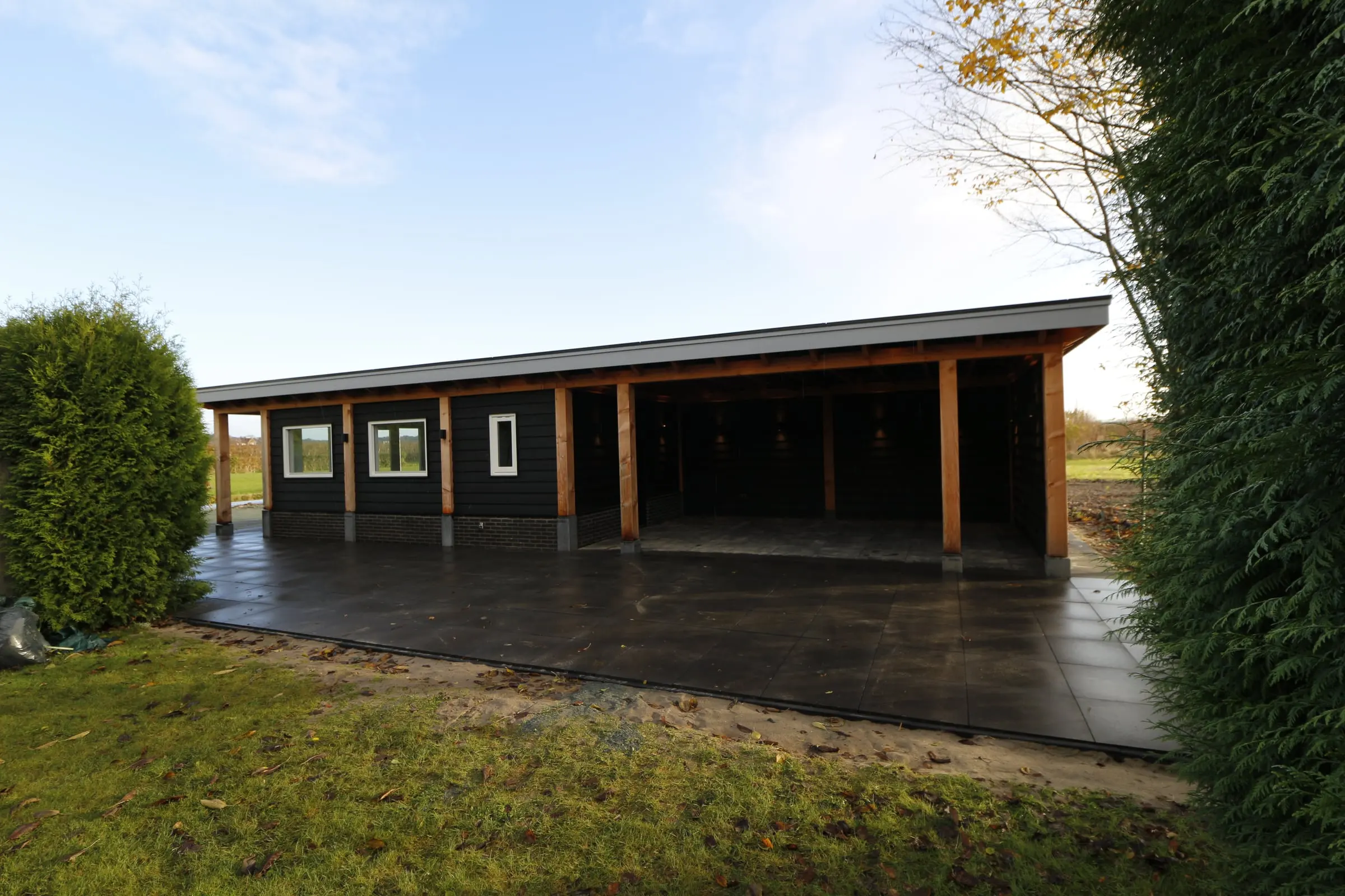 Zwart tuinhuis met een lange open overkapping, gezien vanaf de zijkant
